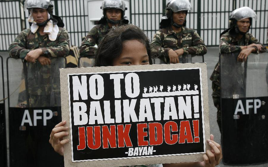 An activist holds a placard in front of Philippine soldiers during a protest rally against the Enhanced Defense Cooperation Agreement (EDCA) image source: Xinhua/Rouelle Umali